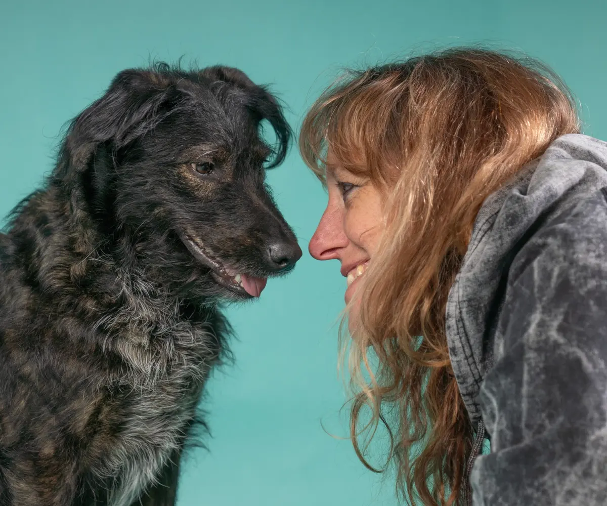 Woman sharing a close moment with a black dog against a teal background