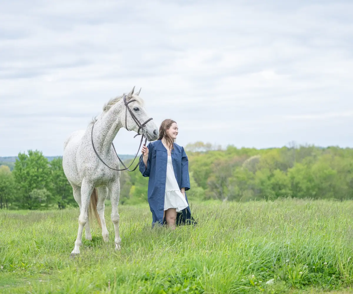 Young woman standing with a white horse in an open field